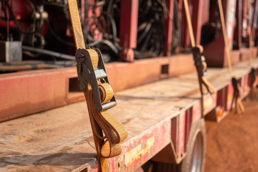 A close-up shot of a heavy-duty yellow ratchet strap securing cargo on the bed of a flatbed trailer.