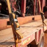 A close-up shot of a heavy-duty yellow ratchet strap securing cargo on the bed of a flatbed trailer.