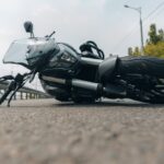 A black motorcycle lying crashed on its side on city asphalt, showing the aftermath of a motorcycle accident road hazards incident.