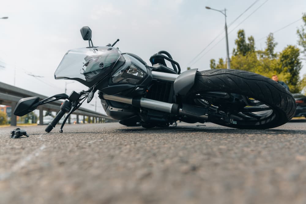 A black motorcycle lying crashed on its side on city asphalt, showing the aftermath of a motorcycle accident road hazards incident.